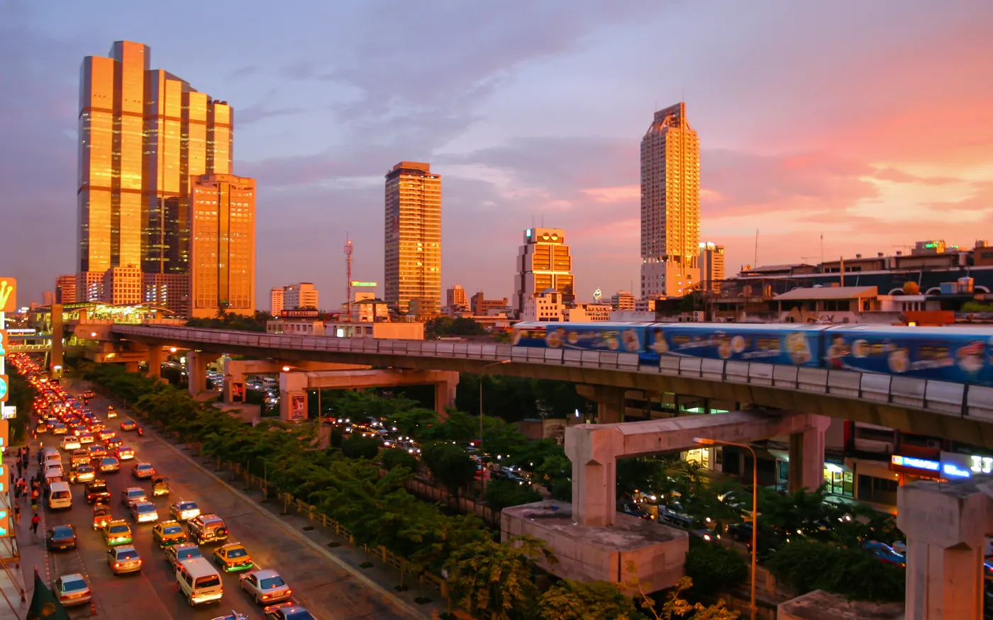 A Skytrain passing over a busy road in Bangkok at sunset