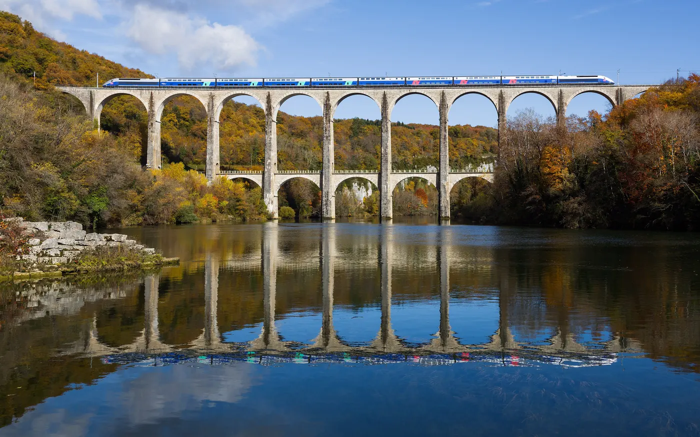A TGV high-speed train crossing a stone viaduct over a river in eastern France