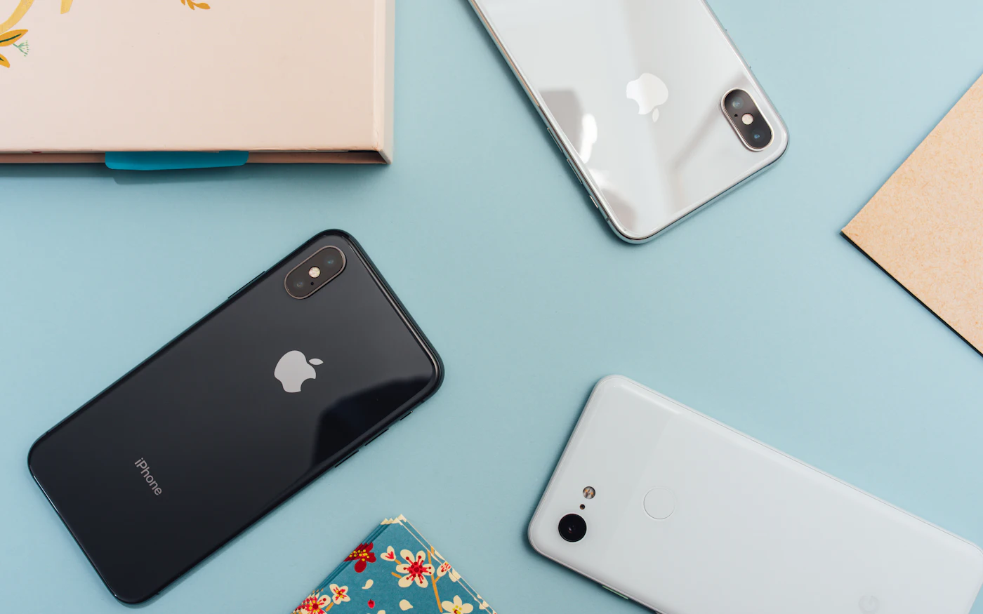 An iPhone and two Android phones lying on a light blue surface
