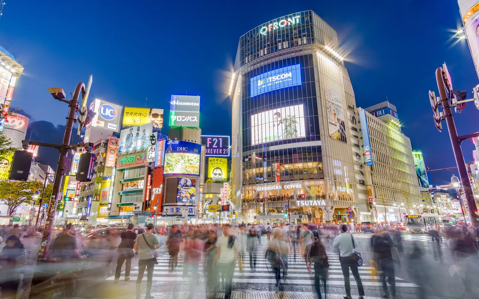Crowds crossing Shibuya Scramble Crossing in Tokyo at dusk, under lit-up screens