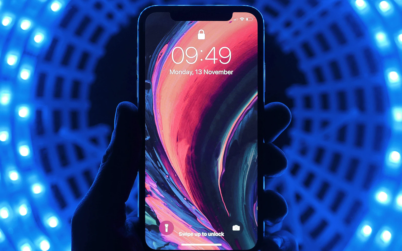 Hand holding a smartphone showing its lock screen against a glowing blue background