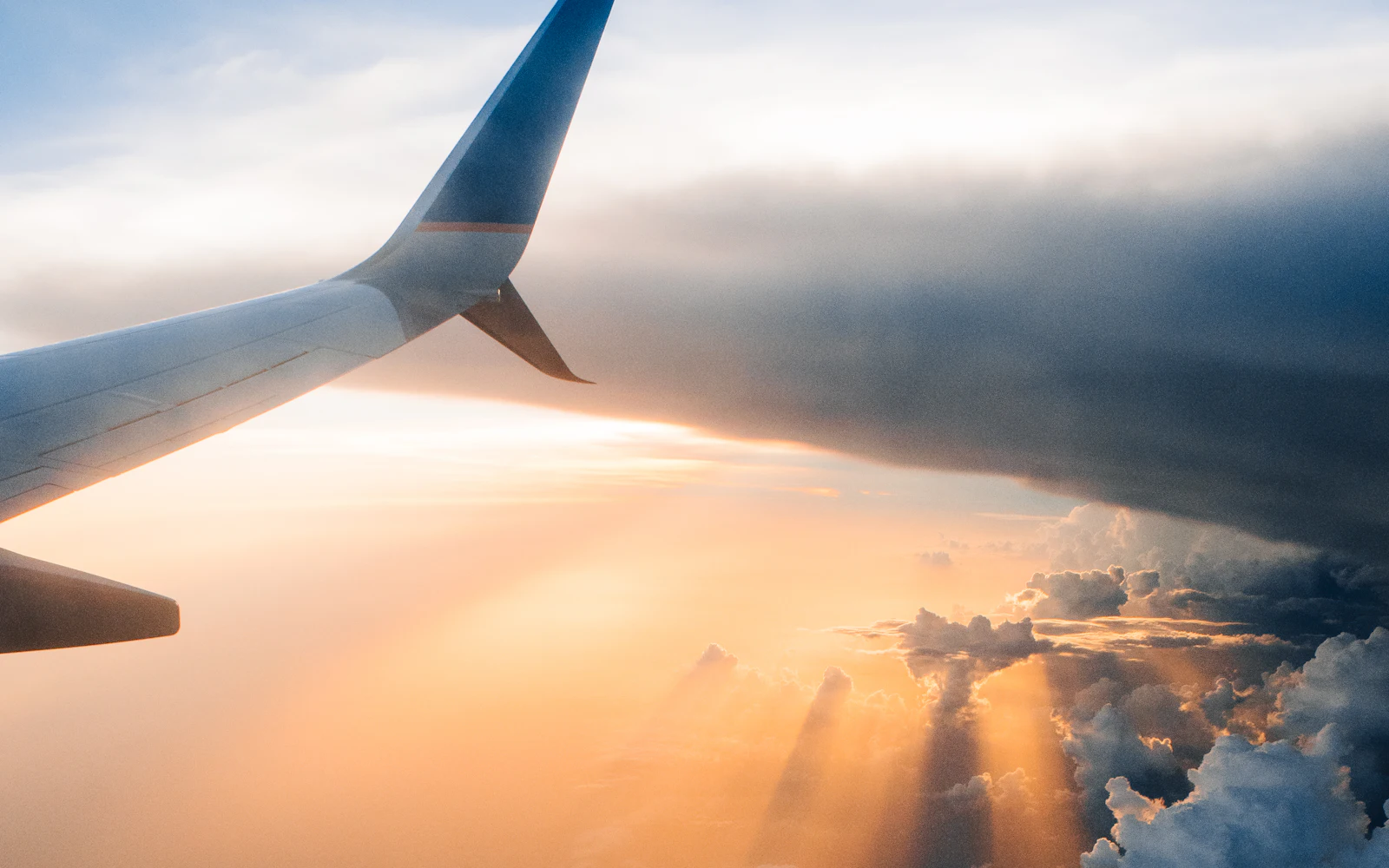 Airplane wing above the clouds with the sun low on the horizon