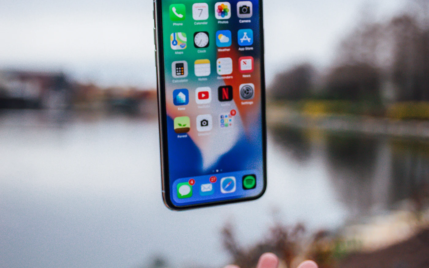 Hand holding up a smartphone against a blurred lakeside background