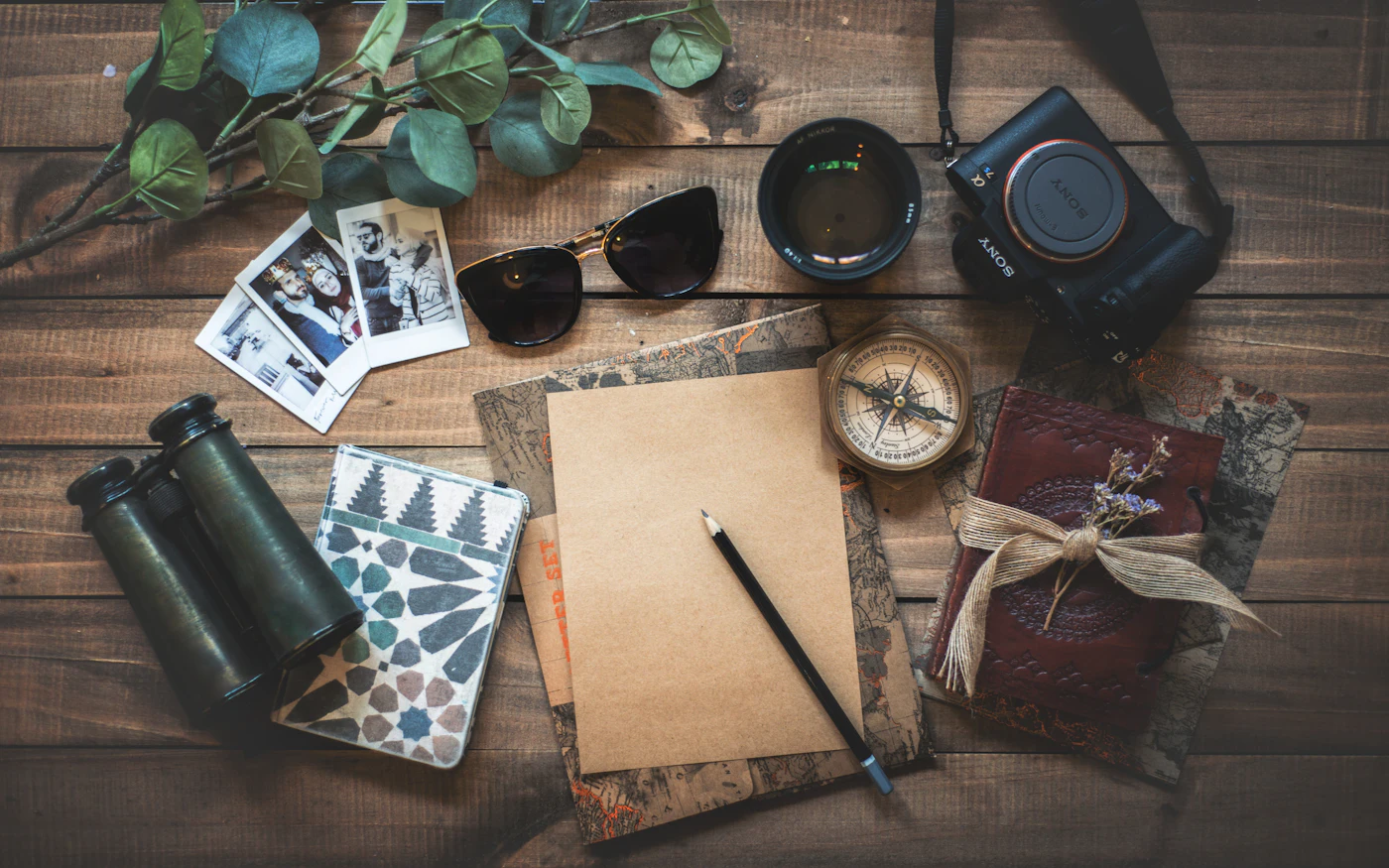 Travel essentials laid out on a wooden table: camera, sunglasses, notebook and compass