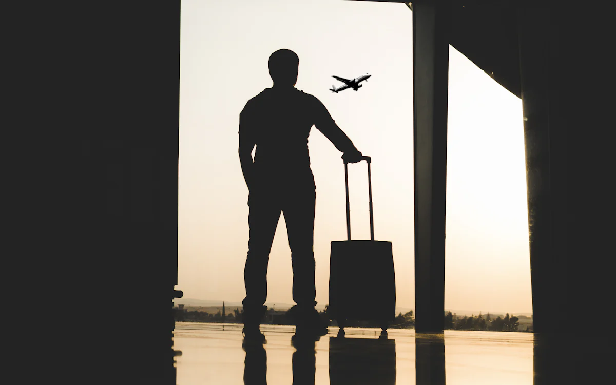 Traveler with a suitcase at an airport window watching a plane take off