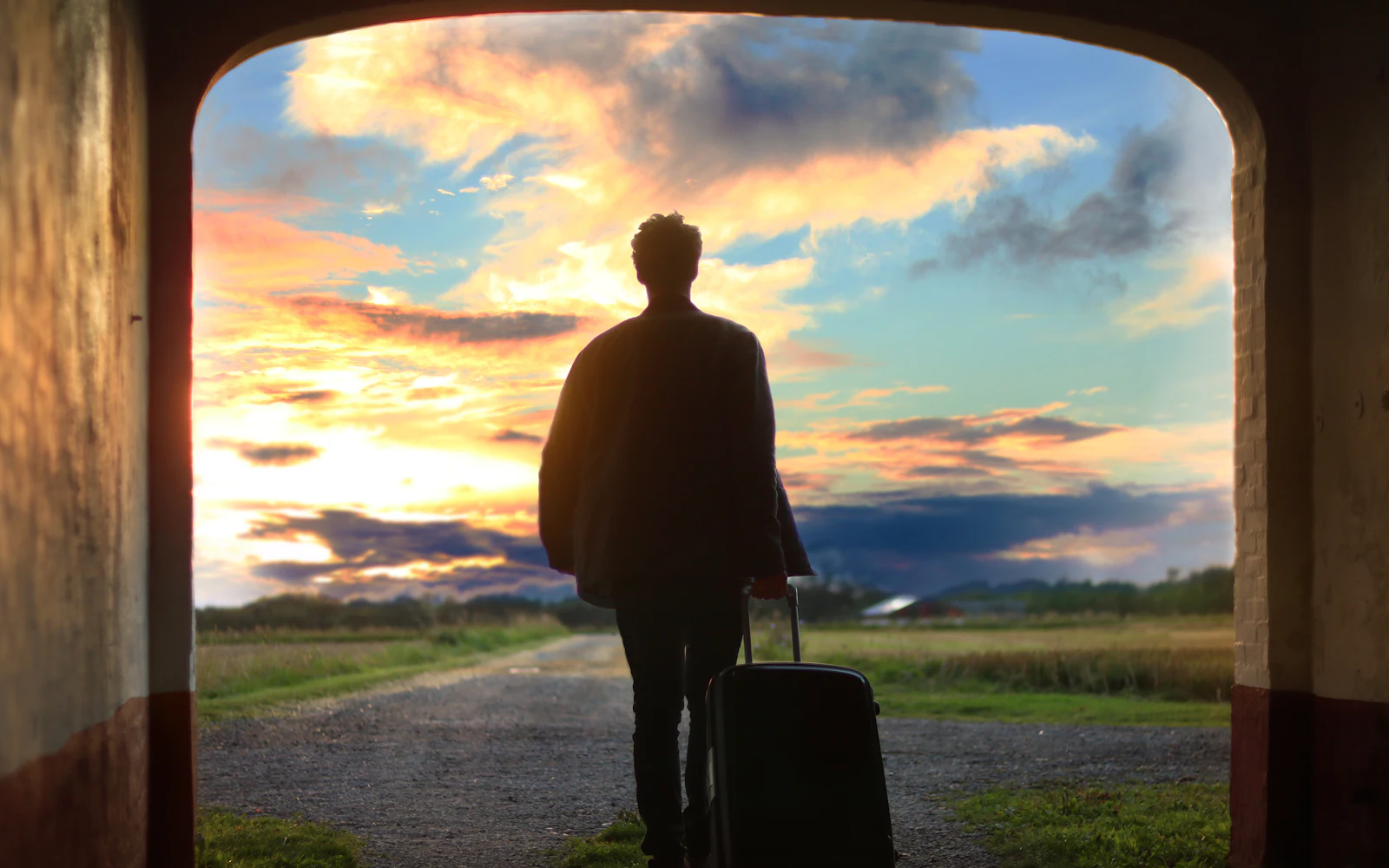Traveler with a suitcase walking through an archway towards a sunset